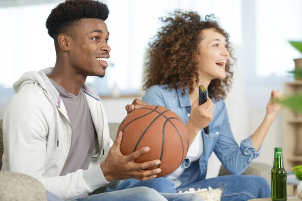 young couple with beer cheering for basketball game at home