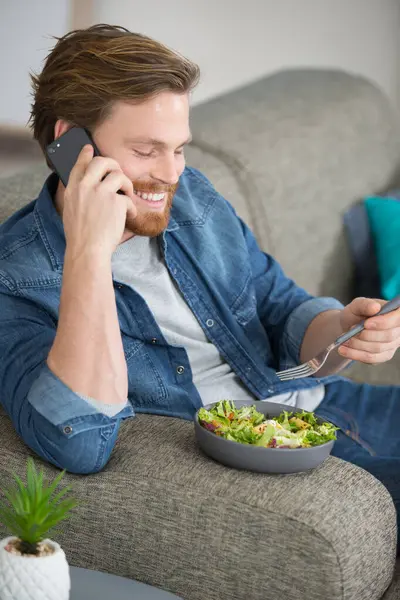Pozytywny Przystojny Mężczyzna Jedzenie Sałatka Podczas Telefon Rozmowa — Zdjęcie stockowe