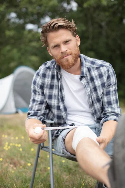 Man Bandaging His Knee While Camping Holiday — Stock Photo, Image
