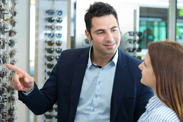 customer in opticians shop choosing frames being guided by salesman
