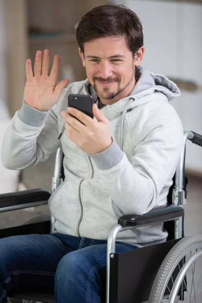 坐在轮椅上的男人在智能手机视频聊天时挥手 — 图库照片
