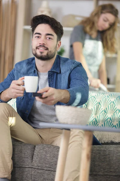 Handsome Man Sitting Remote Control While Wife Ironing — Stock Photo, Image