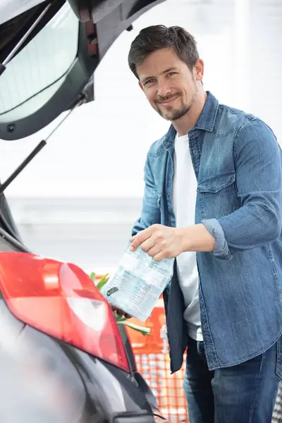 portrait of handsome young man packing groceries into car trunk