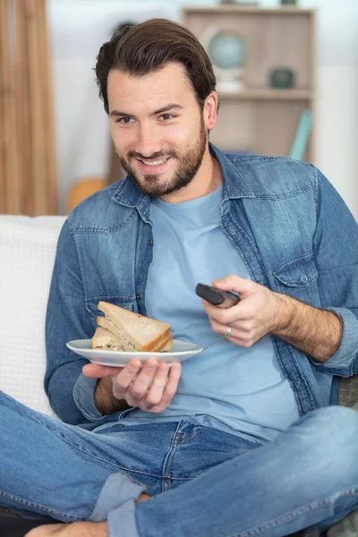 Όμορφος Άντρας Βλέπει Τηλεόραση Ενώ Τρώει Σάντουιτς — Φωτογραφία Αρχείου
