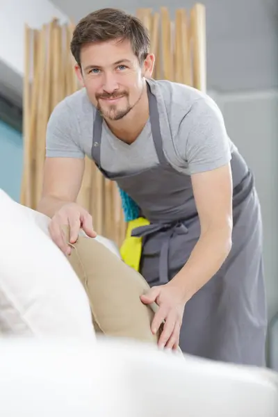 man in apron tidying up le living-room