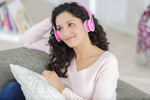 relaxed woman with headphones on sofa at home listening music