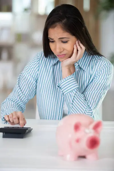 frustrated woman with calculator and piggybank
