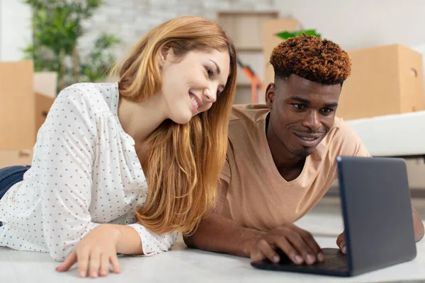 young couple sit on the floor using laptop side view