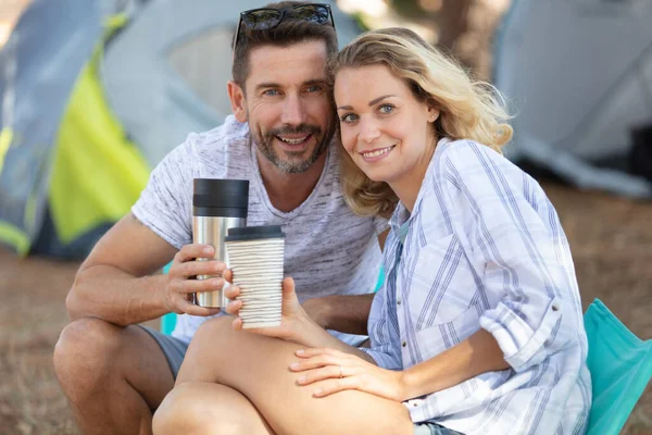 couple on camping trip holding cups by their tent