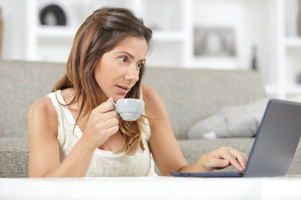 woman with amazed expression drinking coffee and looking his pc
