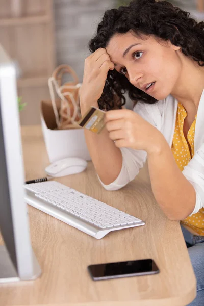 worried young woman using computer and holding credit card
