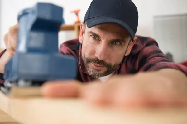 man sanding a wood with sander in a workshop
