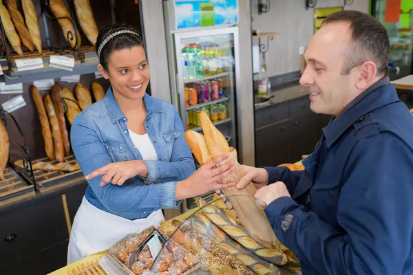man buying fresh baguette from a female baker