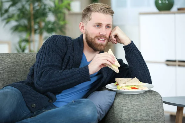テレビの前でサンドイッチを食べるソファーの男 — ストック写真