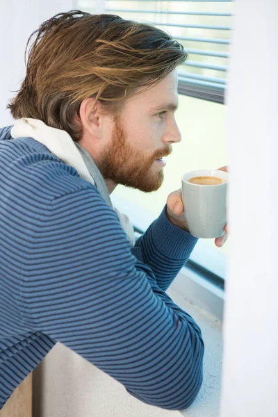 man having his morning coffee while looking through the window