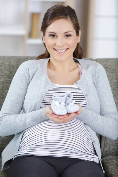 Cheerful Pregnant Sitting Sofa Holding Baby Booties — Stock Photo, Image