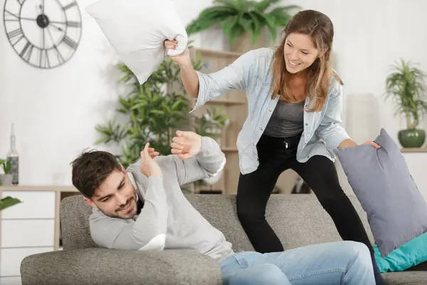 stock image attractive couple fighting with pillows in living room