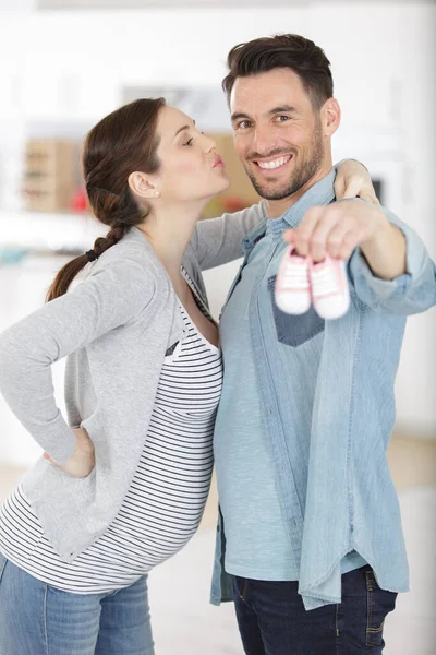 Pregnant Woman Kissing Man Holding Booties — Stock Photo, Image