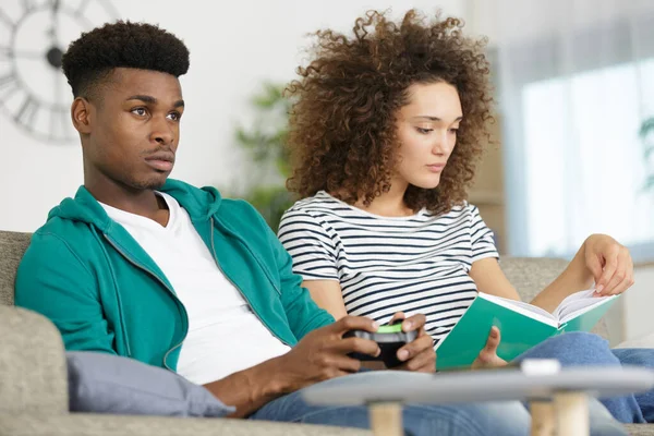 man playing video games and women reading book at home