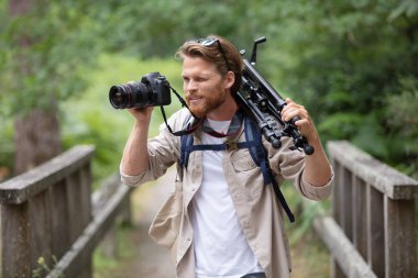 man standing with camera and tripod over his shoulder clipart