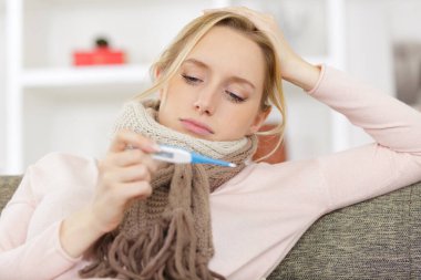 woman lying on couch measuring temperature with thermometer clipart