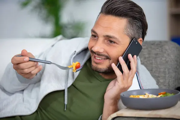 Chico Sentado Sofá Comer Ensalada Mientras Habla Teléfono Inteligente —  Fotos de Stock