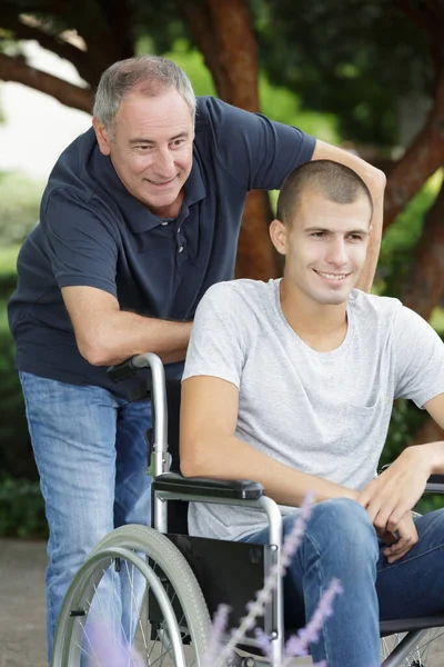 有轮椅束缚的父亲十几岁的儿子在公园里 — 图库照片