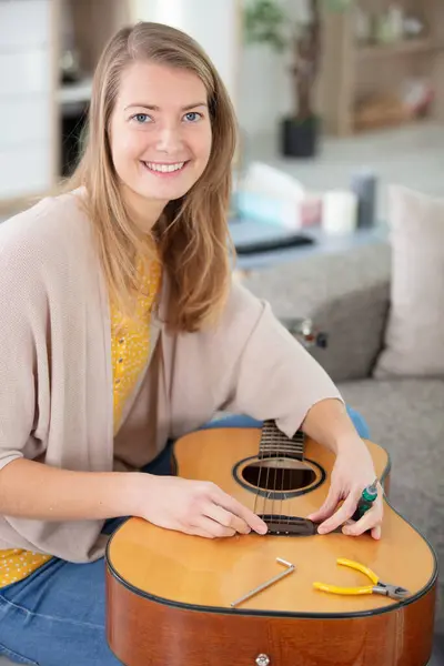 young woman as luthier holds guitar spare part for reparation