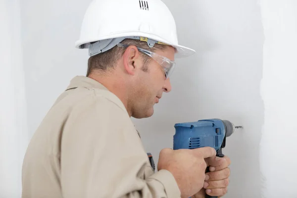 mature tradesman using drill on interior wall