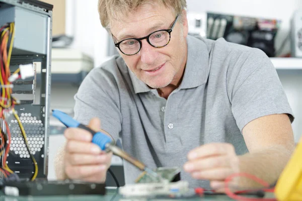 male technician repairing motherboard at table indoors
