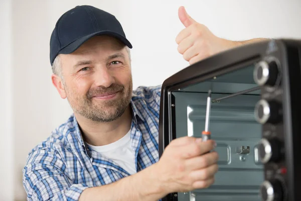 smiling handyman by an electric oven giving thumbs up
