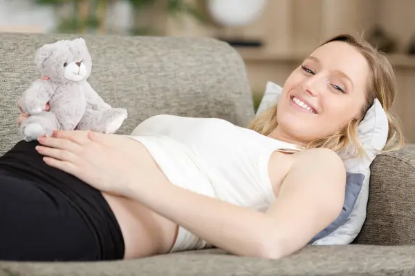 Mujer Embarazada Sonriente Sofá Con Oso Peluche —  Fotos de Stock
