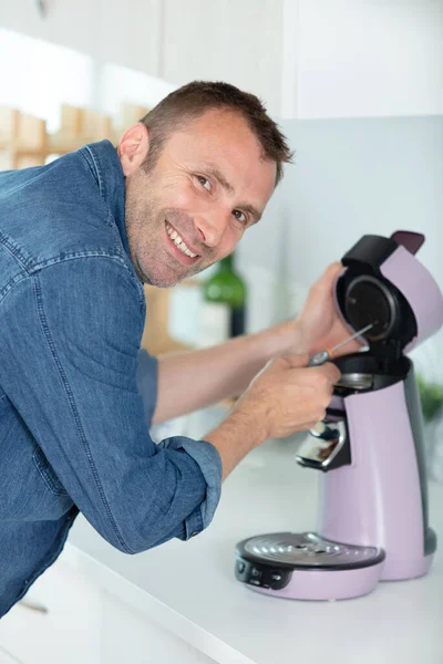 man repairing coffee machine with screwdriver in kitchen