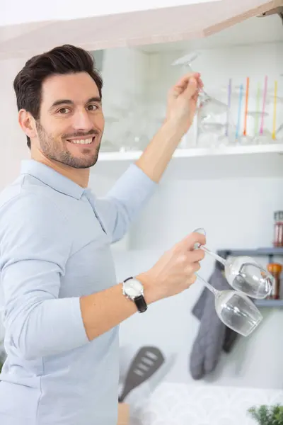 domesticated man puts away glasses in cupboard