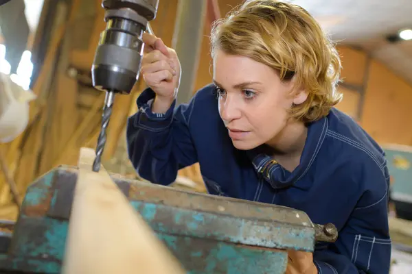 beautiful female carpenter at work using vertical drilling machine