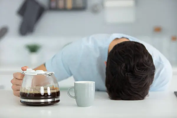 tired man sittingwith jug of coffee and sleeping