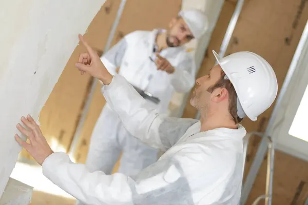 tradesmen in protective clothing inspecting interior wall