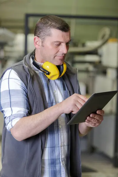 man using tablet pc against industrial equipments in factory