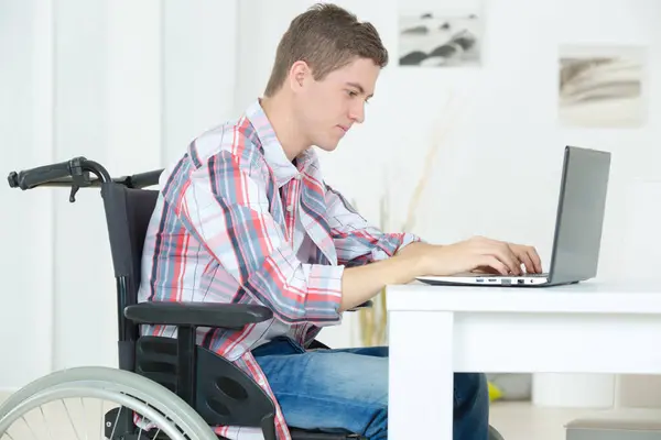 student in wheelchair typing on his laptop in library