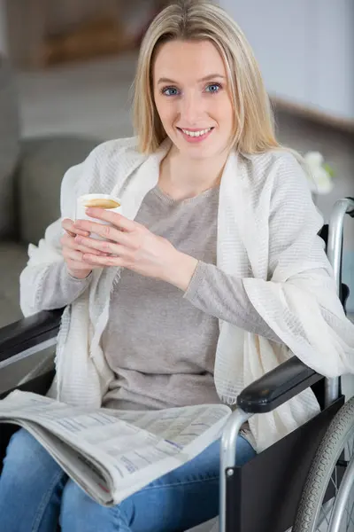 woman in a wheelchair is drinking coffee and reading newspaper