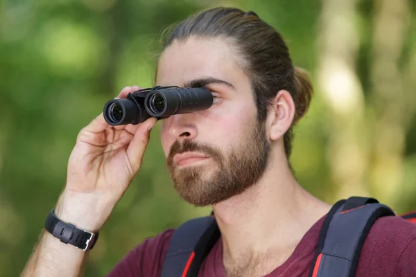 thoughtful man holding binoculars in forest