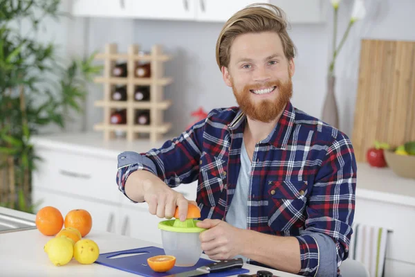 自宅でキッチンでオレンジジュースを作る幸せな男 — ストック写真
