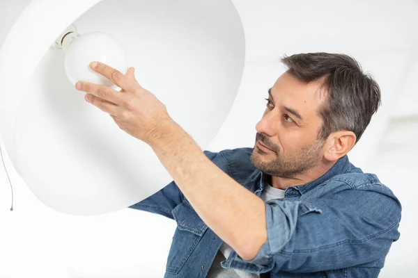 man changing light bulb in pendant lamp indoors