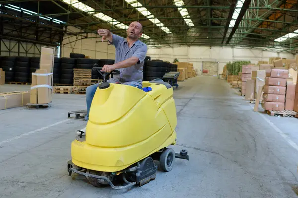 man driving a floor cleaning device in a warehouse