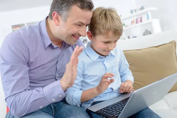 一个男孩和他的爸爸在笔记本电脑上挥手 — 图库照片