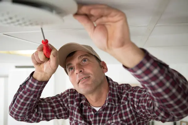 man fitting smoke detector to ceiling