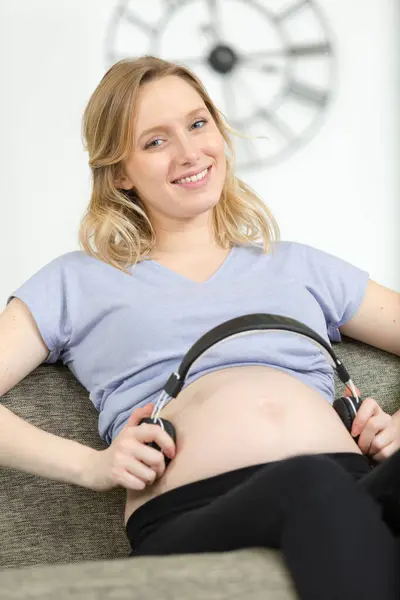 妊娠中の女性は 彼女の腹部にヘッドフォンを置く — ストック写真