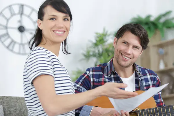 male musician teaches female student how to play guitar