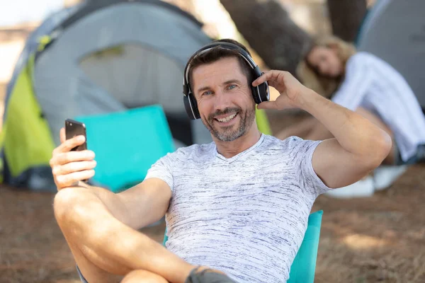Pria Pada Liburan Berkemah Mendengarkan Headphone Melalui Smartphone Nya — Stok Foto