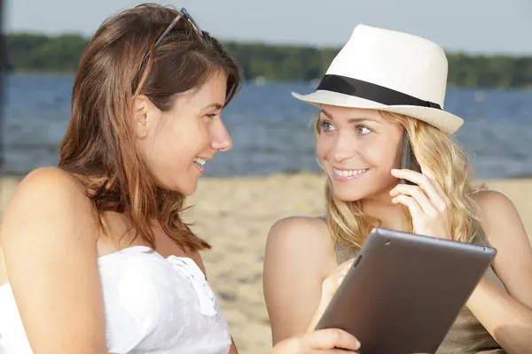 two women talking on the beach using technology